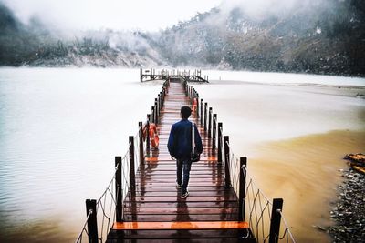 Rear view of man on pier over lake during winter