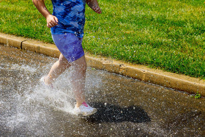 Low section of woman splashing water while walking in puddle