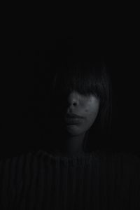 Close-up of teenage girl with obscured face against black background