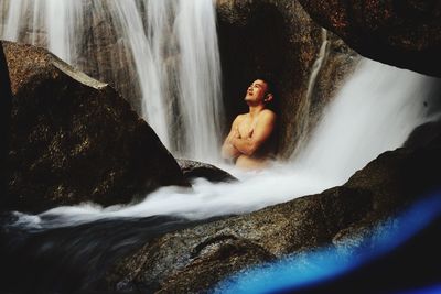 Shirtless man looking at waterfall