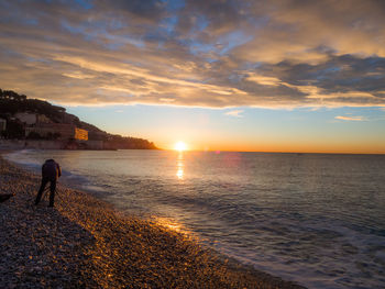 Silhouette man standing on beach against sky during sunset