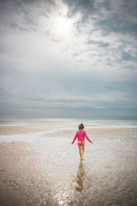 Rear view of girl walking on sandy beach against sky