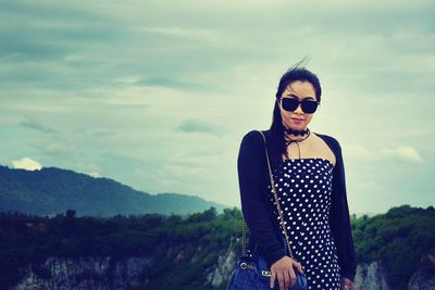 Portrait of beautiful young woman standing by tree against sky