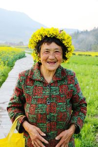 Portrait of happy senior woman wearing flower wreath on field