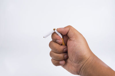 Close-up of hand holding cigarette over white background