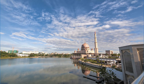 Mosque by lake against cloudy sky