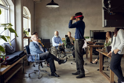 Male and female colleagues watching businessman wearing vr simulator at office