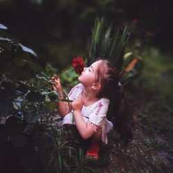 Girl smelling rose while crouching on field