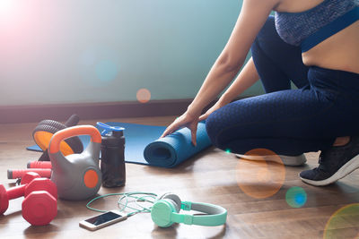 Low section of woman rolling exercise mat on hardwood floor
