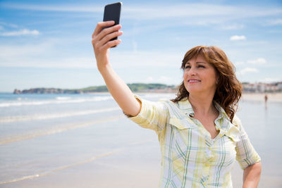 Smiling woman taking selfie on mobile phone at beach