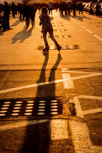 Rear view of woman inline skating towards crowd on street at sunset