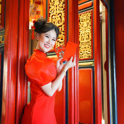 Young woman holding red door at entrance