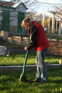 Side view of woman using weed trimmer in yard