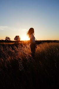 Teenage girl holding camera while standing on grassy field during sunset