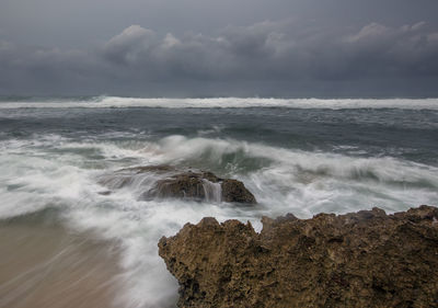 Long exposure image of waves crashing at beach against storm clouds