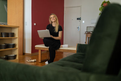 Woman working at home from couch with laptop on her lap. home office concept. gray notebook