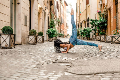 Young woman exercising on footpath amidst buildings