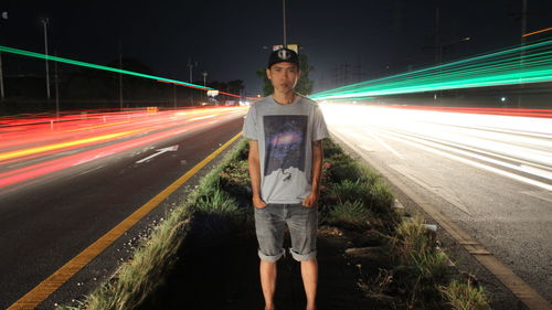 Portrait of young man standing amidst light trails in city