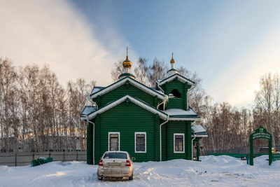 Snow covered house by building against sky