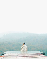Rear view of man sitting on mountain against sky