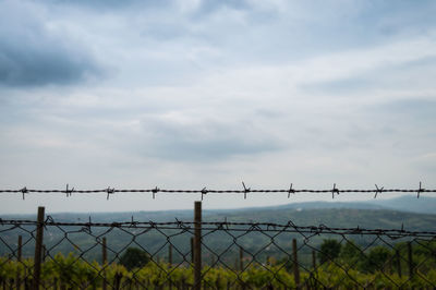 Barbed wire fence against cloudy sky