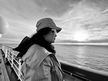 Woman wearing sunglasses while standing by railing of boat in sea against sky