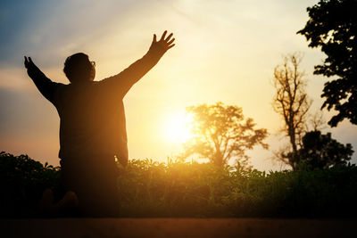 Rear view of silhouette man standing by tree against sky during sunset