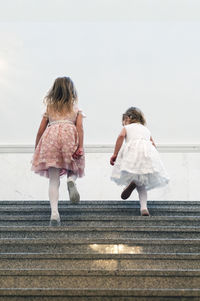 Low angle view of sisters moving up steps against wall