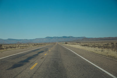 Road amidst desert against clear blue sky