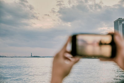 Man photographing through mobile phone in sea against sky