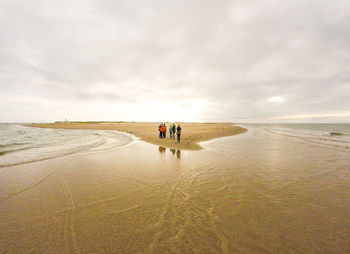 Rear view of people walking on beach against sky