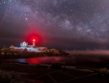 Lighthouse on rock by river against sky at night