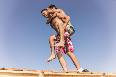 Low angle view of friends standing against clear blue sky