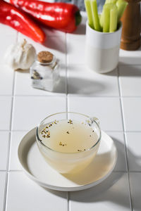 Healthy golden bone broth with spices in a mug on a saucer on a white background. 