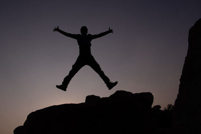 Silhouette man jumping on rock against sky during sunset