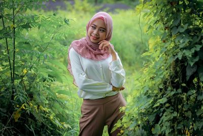 Portrait of young woman standing against plants