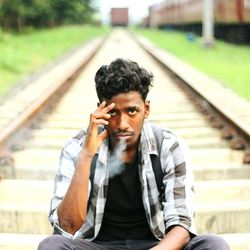 Portrait of young man exhaling smoke while sitting on railroad track