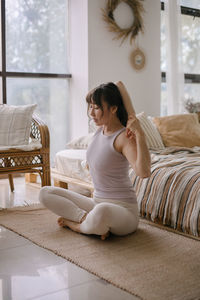 Young woman using phone while sitting on bed at home