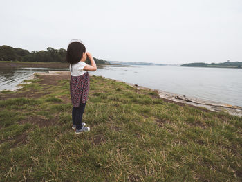 Girl standing on lakeshore against sky