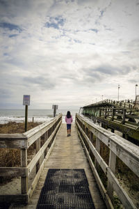 Rear view of woman walking on footbridge against sea