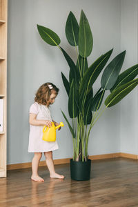 Little girl waters flowers at home, helps care for plants