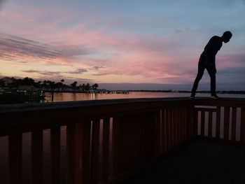 Silhouette man standing by railing against sky during sunset