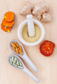 Directly above shot of ginger with powder and turmeric by capsules on table