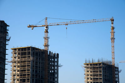 Low angle view of crane by building against clear sky