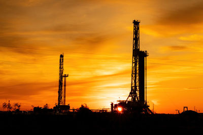 Silhouette drilling rigs against sky during sunset