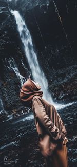 Low angle view of shirtless man on rock at waterfall