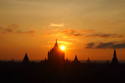 Silhouette temple against buildings during sunset