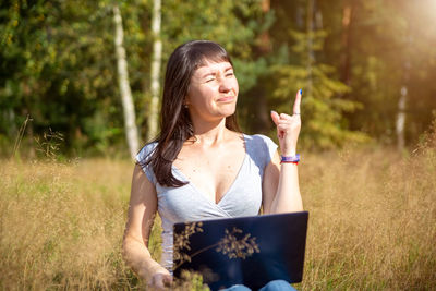 Portrait of young woman using mobile phone while sitting on field