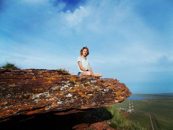 Young woman sitting on rock by sea against sky