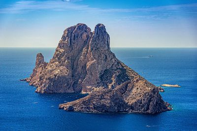 Rock formation by sea against blue sky